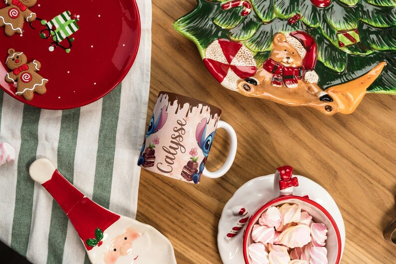 May include: A festive holiday scene with a red plate featuring gingerbread men and a gift, a Christmas tree-shaped serving dish, and a mug with a cartoon character design. A Santa-shaped dish and a bowl of marshmallows complete the arrangement.