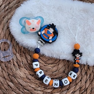 May include: A baby pacifier and a pacifier clip with the name "PREZMO" spelled out in white lettered beads. The pacifier has a blue and white design with a bear face. The clip features a Dragon Ball Z character.