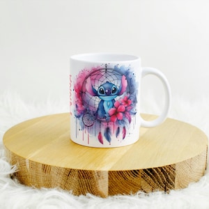 K&ouml;nnte beinhalten: Wei&szlig;e Keramiktasse mit einer Aquarellillustration von Stitch aus Lilo & Stitch in einem Traumf&auml;nger-Design. Das Design umfasst rosa und blaue Akzente, Blumen und Federn. Die Tasse hat einen gebogenen Griff.
