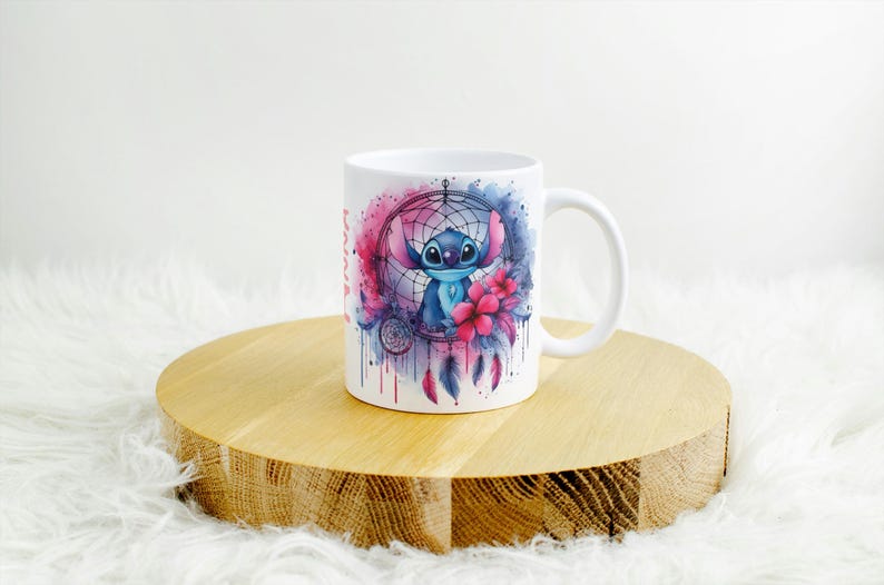 K&ouml;nnte beinhalten: Wei&szlig;e Keramiktasse mit einer Aquarellillustration von Stitch aus Lilo & Stitch in einem Traumf&auml;nger-Design. Das Design umfasst rosa und blaue Akzente, Blumen und Federn. Die Tasse hat einen gebogenen Griff.