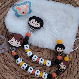 Puede incluir: Pinzas para chupetes de bebé con diseños de personajes de Harry Potter. Los clips tienen cuentas negras, naranjas, amarillas y blancas que deletrean "HARRY". Los chupetes tienen un diseño de oso azul y blanco.