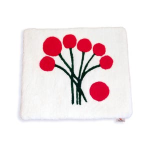 May include: A white, rectangular decorative pillow with a plush texture. The pillow features a design of red circular shapes on green stems, resembling a stylized floral arrangement. The design is centered on the pillow.