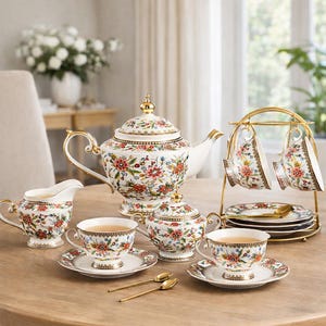 Könnte beinhalten: Ein komplettes Blumenservice mit weißer Basis und goldenen Akzenten. Das Set beinhaltet eine Teekanne, eine Zuckerdose, einen Sahnekännchen, Tassen, Untertassen und Löffel. Die Tassen werden auf einem goldenen Ständer präsentiert. Blumenmuster in Rot, Rosa und Grün.