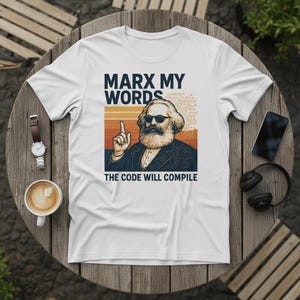 Peut inclure: T-shirt blanc avec un motif de Karl Marx portant des lunettes de soleil, avec le texte "MARX MY WORDS" au-dessus et "THE CODE WILL COMPILE" en dessous. Le design comprend des rayures orange et marron.