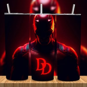 May include: A tumbler featuring a red and black graphic of a superhero. The design includes the character's silhouette, a red costume, and the letters "DD" in a bold font. The tumbler has a silver straw.