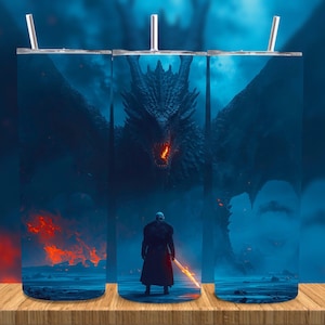 May include: A stainless steel tumbler featuring a fantasy scene with a dragon and a figure holding a glowing sword. The artwork is predominantly blue with fiery orange accents, creating a dramatic and epic feel. The tumbler includes a straw.