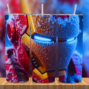Könnte beinhalten: Drei Edelstahlbecher mit einem Nahaufnahme-Design von Iron Mans Helm. Das Design ist rot, gold und gelb, mit blau leuchtenden Augen und einem Schneeeffekt. Jeder Becher hat einen silbernen Strohhalm.