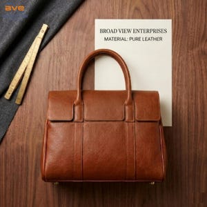 May include: A brown leather handbag with a top handle and a rectangular shape. The bag has a flap closure and vertical stitching details. The text on the paper reads: BROAD VIEW ENTERPRISES MATERIAL: PURE LEATHER.