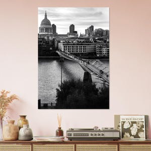 Può includere: Fotografia in bianco e nero di un paesaggio urbano con un ponte su un fiume. Si vedono persone che attraversano il ponte. Un grande edificio a cupola e altri edifici si ergono sullo sfondo.