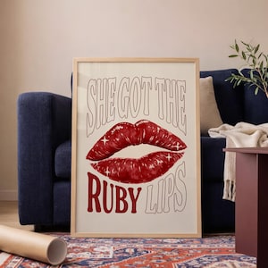 Pode incluir: Uma impressão artística emoldurada com lábios vermelhos e estrelas, com o texto "SHE GOT THE RUBY LIPS" em uma fonte retrô. A obra de arte é exibida em uma moldura de madeira clara, adicionando um toque vintage.