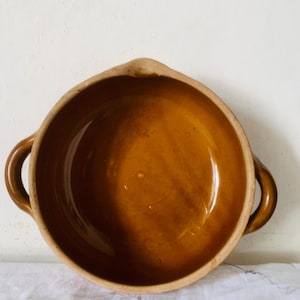 Puede incluir: Una taza de cerámica blanca con asa negra y el texto "But First, Coffee" en negrita negra. La taza está llena de un líquido oscuro, probablemente café, y se encuentra sobre una superficie clara.