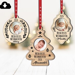 Pode incluir: Três enfeites de Natal de madeira com fotos de bebês. Um é redondo, outro em forma de árvore e outro em forma decorativa. Cada um tem uma fita vermelha e o texto "MEIN ERSTES WEIHNACHTEN" com um nome e o ano de 2026.