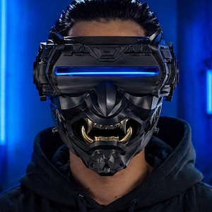 Op de afbeelding: Zwarte VR-headset met een op samurai geïnspireerd ontwerp. De headset heeft een blauw gloeiend licht en goudkleurige tanden. De afbeelding staat tegen een blauwe achtergrond.
