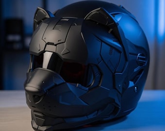 May include: A matte black motorcycle helmet with a unique cat-like design. The helmet features integrated ears, a nose-shaped visor, and a dark visor. The design incorporates angular, geometric shapes, giving it a futuristic aesthetic.