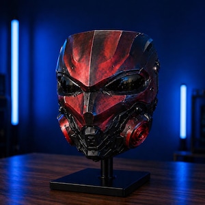 May include: A futuristic, red and black mask with a detailed design, featuring dark lenses and circular accents. The mask is displayed on a black stand against a blue-lit background, showcasing a sci-fi or cosplay theme.