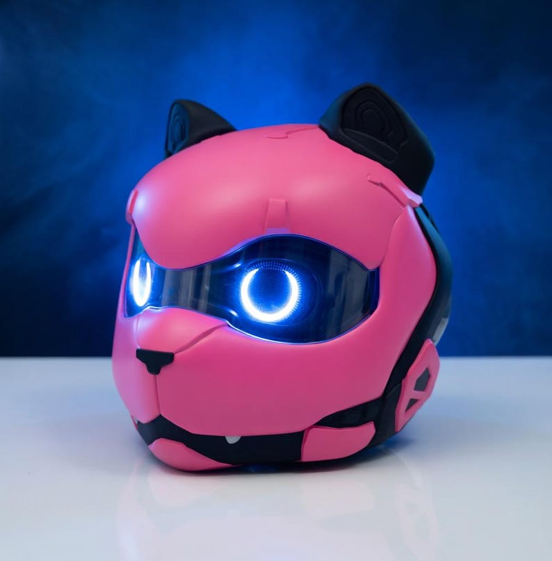 May include: A pink robotic cat head with black detailing and ears. The cat's eyes emit a bright blue light. The design has a futuristic aesthetic, with smooth, rounded surfaces and a sleek appearance. The background is a gradient of blue.