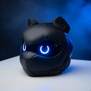 May include: A black, cat-shaped device with glowing blue accents. The device has a sleek, futuristic design with a cat-like face, ears, and glowing, crescent-shaped eyes. The device is likely a speaker or a smart home device.