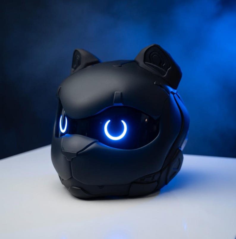 May include: A black, cat-shaped device with glowing blue accents. The device has a sleek, futuristic design with a cat-like face, ears, and glowing, crescent-shaped eyes. The device is likely a speaker or a smart home device.