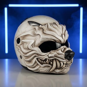 Op de afbeelding: Witte motorhelm met een wolfachtig ontwerp. De helm heeft een zwart vizier, een zwarte neus en gedetailleerde tanden. Het ontwerp is gebeeldhouwd om op een wolvengezicht te lijken, met ingewikkelde vachtachtige texturen.