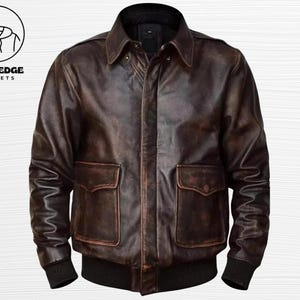 Könnte beinhalten: Braune Lederjacke mit zwei Vordertaschen, Kragen und schwarzen gerippten Bündchen und Saum. Die Jacke hat ein Used-Look-Design und den Text "BOLD EDGE JACKETS" in einem kreisförmigen Logo.