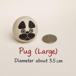 May include: A beige, egg-shaped decorative item with a pug face painted on it. The pug's face features black markings around the eyes, ears, and snout. The text "Pug (Large)" and "Diameter about 3.5 cm" is below the item.