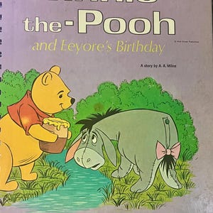 May include: A vintage children's book cover with the title "Winnie-the-Pooh and Eeyore's Birthday". The cover is light purple, and features illustrations of Winnie-the-Pooh and Eeyore. Winnie is holding a honey pot, and Eeyore has a pink bow.