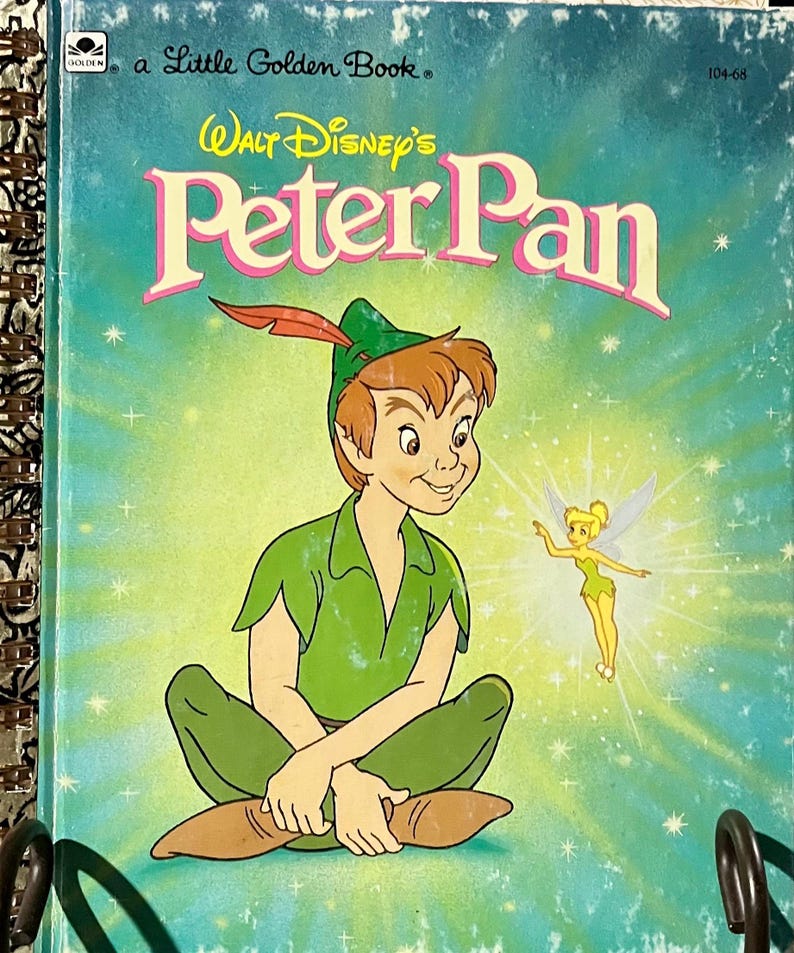 May include: A Little Golden Book titled Walt Disney's Peter Pan, featuring an illustration of Peter Pan in a green outfit with a red feather in his cap, sitting cross-legged next to a small Tinker Bell, set against a bright teal background.