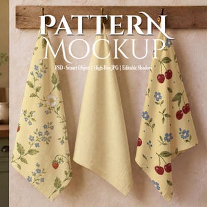 May include: Three hanging kitchen towels displayed on a wooden rack. The left towel features a strawberry and floral pattern, the centre towel is solid pale yellow, and the right towel displays a cherry and blue flower pattern on a yellow background.