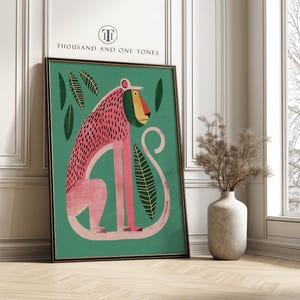 May include: A framed art print with a monkey illustration in pink and green. The monkey has a pink body, a red and yellow face, and is set against a green background with green leaves. The text "THOUSAND AND ONE TONES" is at the top of the print.