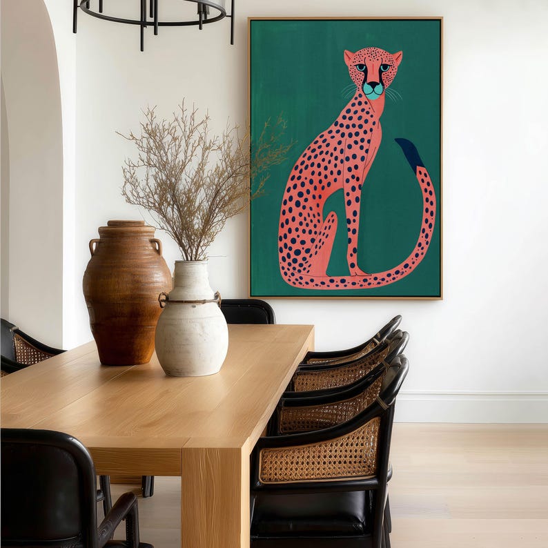 Stylized art print of a pink spotted cheetah on deep green, large framed above a light wood dining table in an airy dining room with cane-back chairs and ceramic vases.