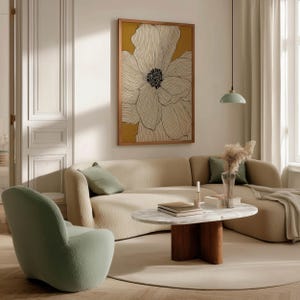 Minimal floral wall art print with ivory petals on mustard yellow, cozy modern vibe, framed art print displayed above a curved sofa in a living room.