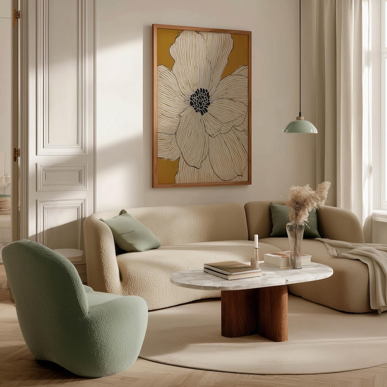 Minimal floral wall art print with ivory petals on mustard yellow, cozy modern vibe, framed art print displayed above a curved sofa in a living room.