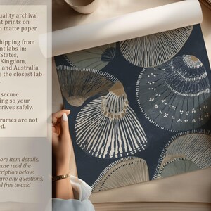 Textured seashell art print in navy and neutral beige, shown being unrolled on a tabletop beside a cup with an overlay about matte paper and secure packaging.
