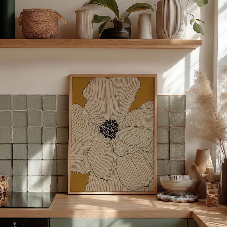 Simple botanical bloom in cream on warm yellow with black center, modern poster style, framed wall art print styled on a kitchen counter by tile.