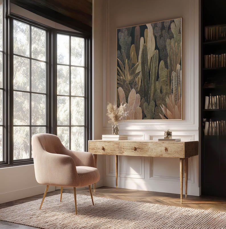 Lush stylized succulents and cacti in olive and tan, framed art print above a rustic wooden desk in a bright home office with a blush lounge chair.