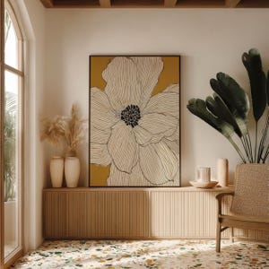 Oversized flower line drawing in white and ochre with dark center, calm modern mood, framed poster centered above a low cabinet in a bright corner.