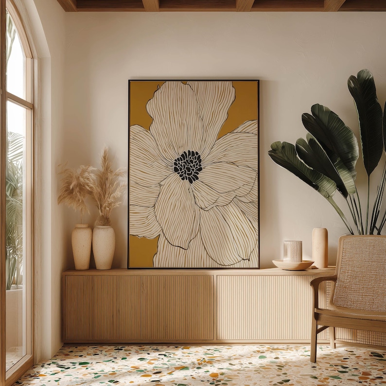 Oversized flower line drawing in white and ochre with dark center, calm modern mood, framed poster centered above a low cabinet in a bright corner.