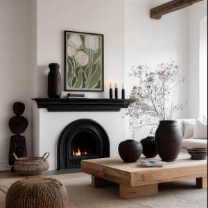 Cozy green floral wall art print with cream petals and a warm contemporary mood, framed above a black fireplace mantel in a neutral living room with woven accents and a lit fire.
