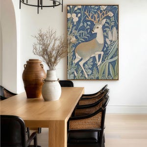 Enchanting forest stag in blue and cream hues with surrounding flowers wall art print is displayed large above a light wood dining table in an airy dining room.