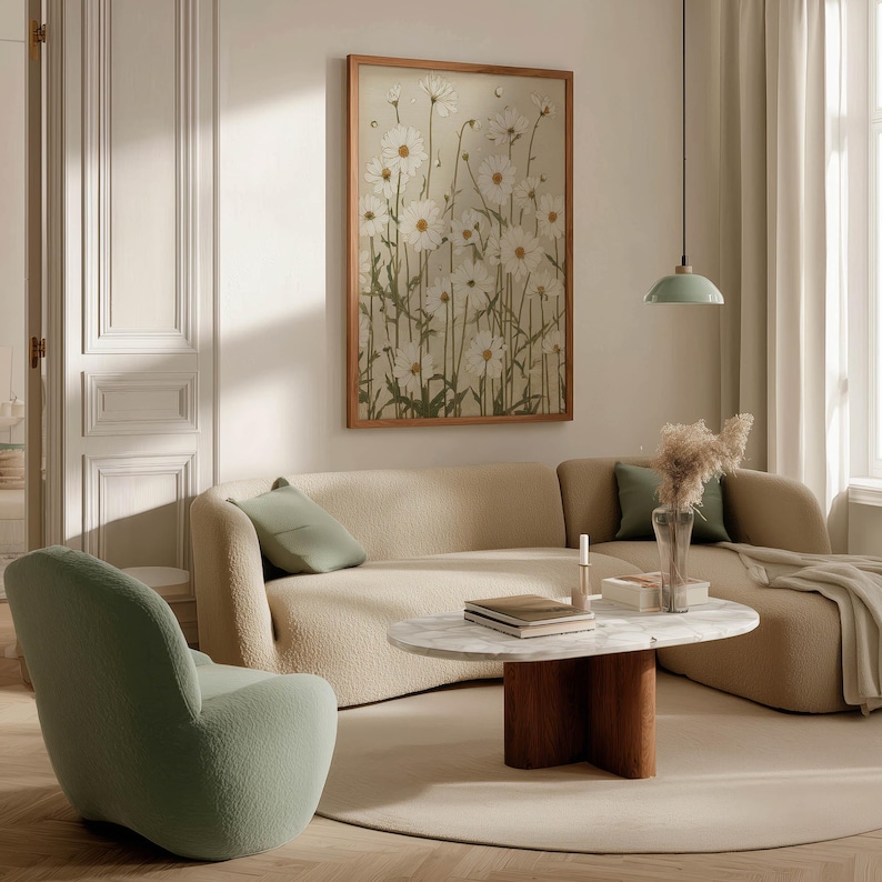 Charming vintage botanical art print of white daisy flowers on a beige textured background, hung above a curved sofa with books, coffee table, and pendant lamp.
