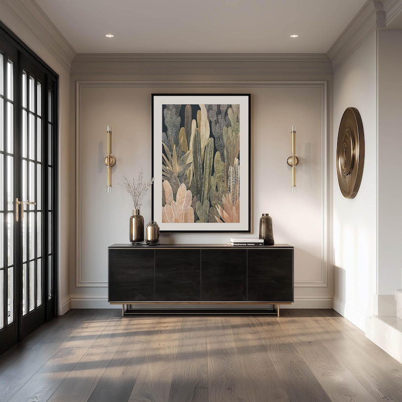 Neutral earth-tone cactus illustration in olive and cream, large framed art print above a sleek black console in an elegant entryway with brass accents and glass doors.