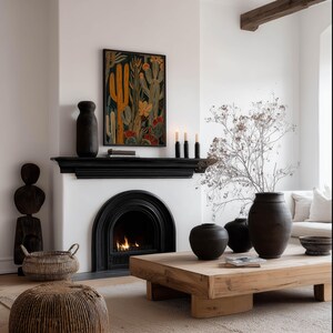 Muted desert botanical art print in deep black, yellow and rust, inviting mood; framed art print above a black fireplace mantel in a cozy neutral living room with a lit fire and woven accents.