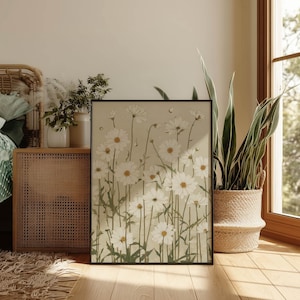 Airy floral art print featuring white daisy blooms and muted green stems on warm beige, styled in a cozy bedroom corner by a woven cabinet and sunny window.