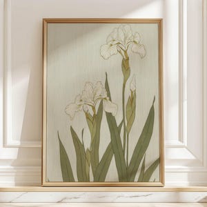 May include: A framed botanical print depicting white iris flowers with green stems and leaves. The artwork is set against a light green background and framed in a gold-coloured frame. The print is displayed on a white surface.