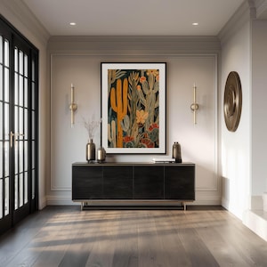 Detailed desert botanical art print in dark background with mustard and rust accents, rich layered mood; large framed art print above a sleek black console in an elegant entryway with brass wall decor and double glass doors.