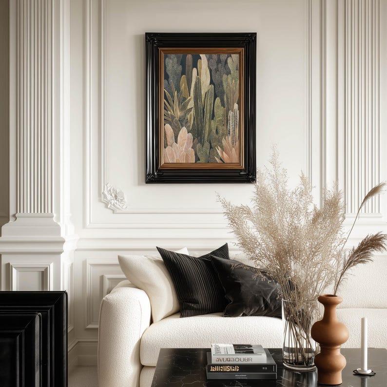 Elegant cactus and leaf illustration in neutral hues, framed art print centered on an ornate paneled wall above a cream sofa styled with pampas grass.