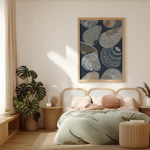 Oversized seashell art print featuring fan shells on a deep navy background with neutral accents, hanging above a cane headboard with green bedding in gentle daylight.