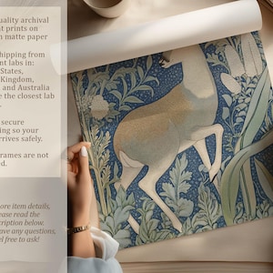 Detailed blue woodland deer botanical art print is being unrolled on a neutral tabletop by two hands, with text highlighting archival pigment inks and matte paper.