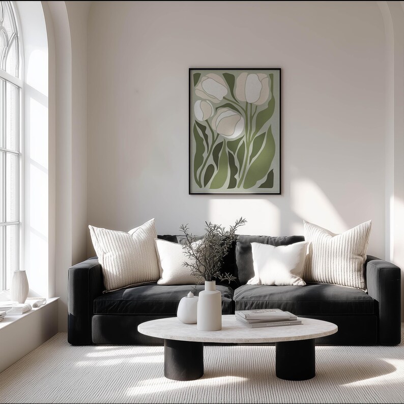 Minimal green floral poster in muted sage and cream with a clean contemporary mood, framed on a soft white wall in a bright living room with a black sofa and arched window.