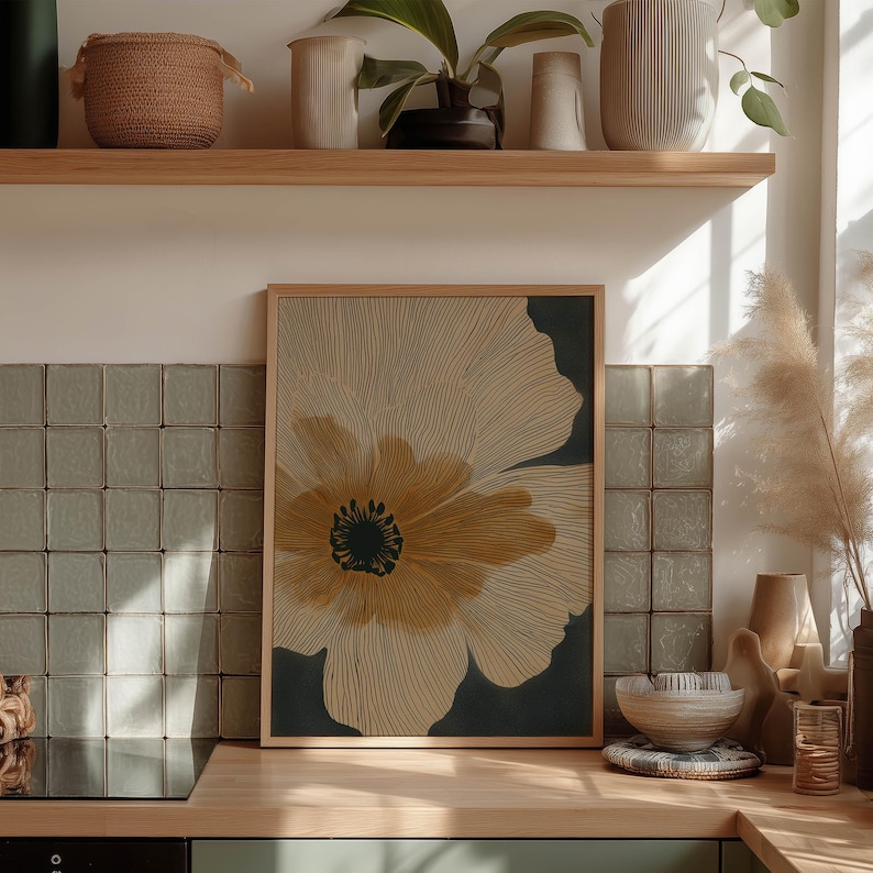 Modern botanical wall art print with a large beige bloom and dark background, warm golden center and crisp linework, framed on a kitchen counter vignette.